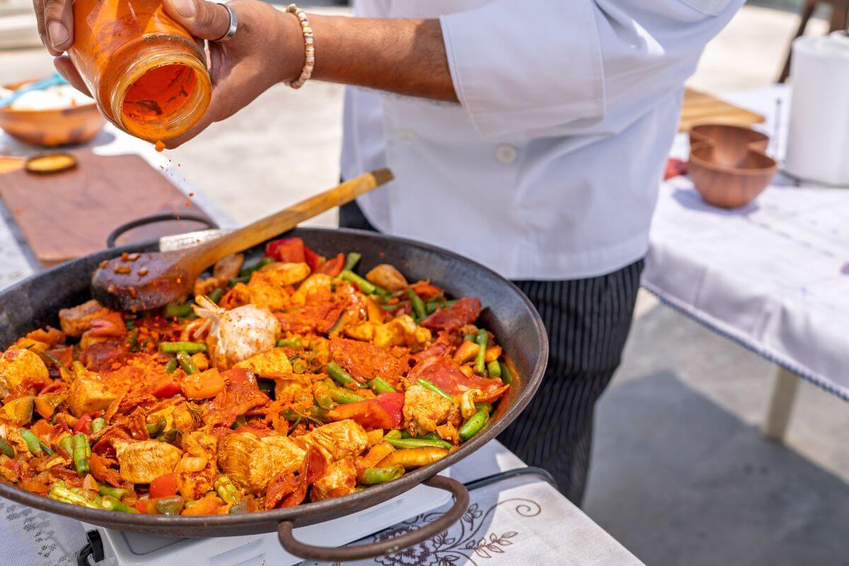 Un traiteur entrain de rajouter des épices dans une paella